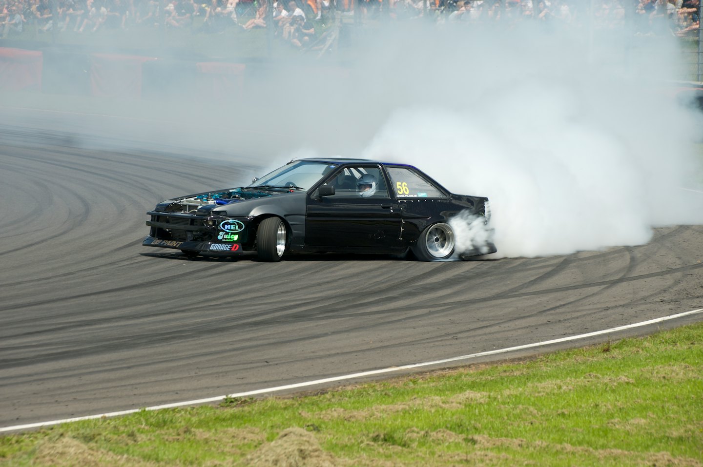 Modified black car drifting on an asphalt race track.