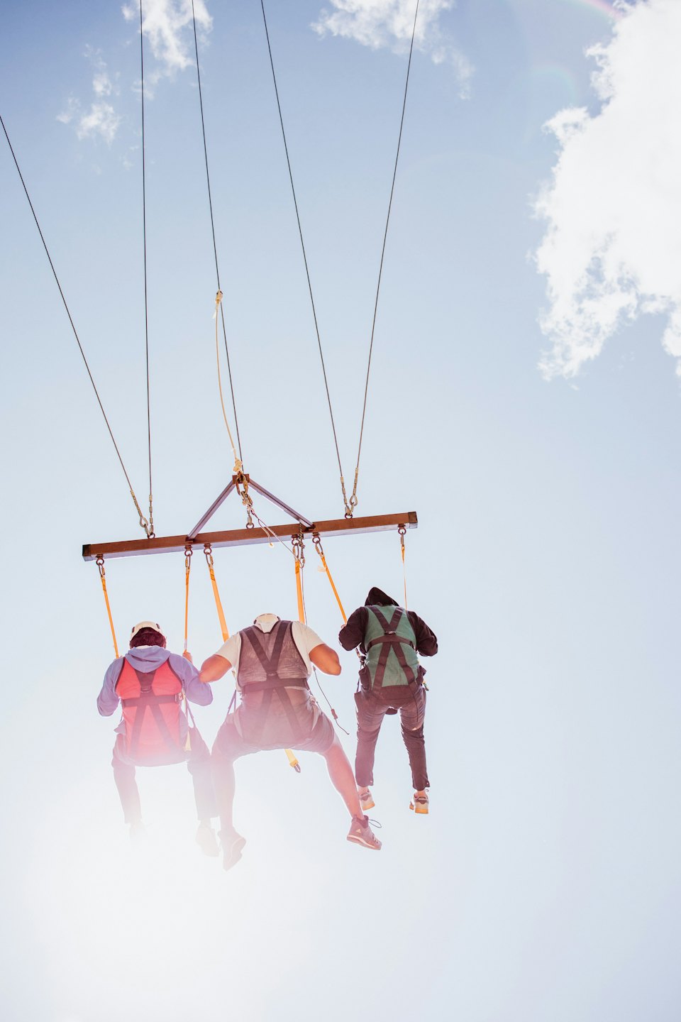 Three people in safety harnesses hang from a wooden beam.