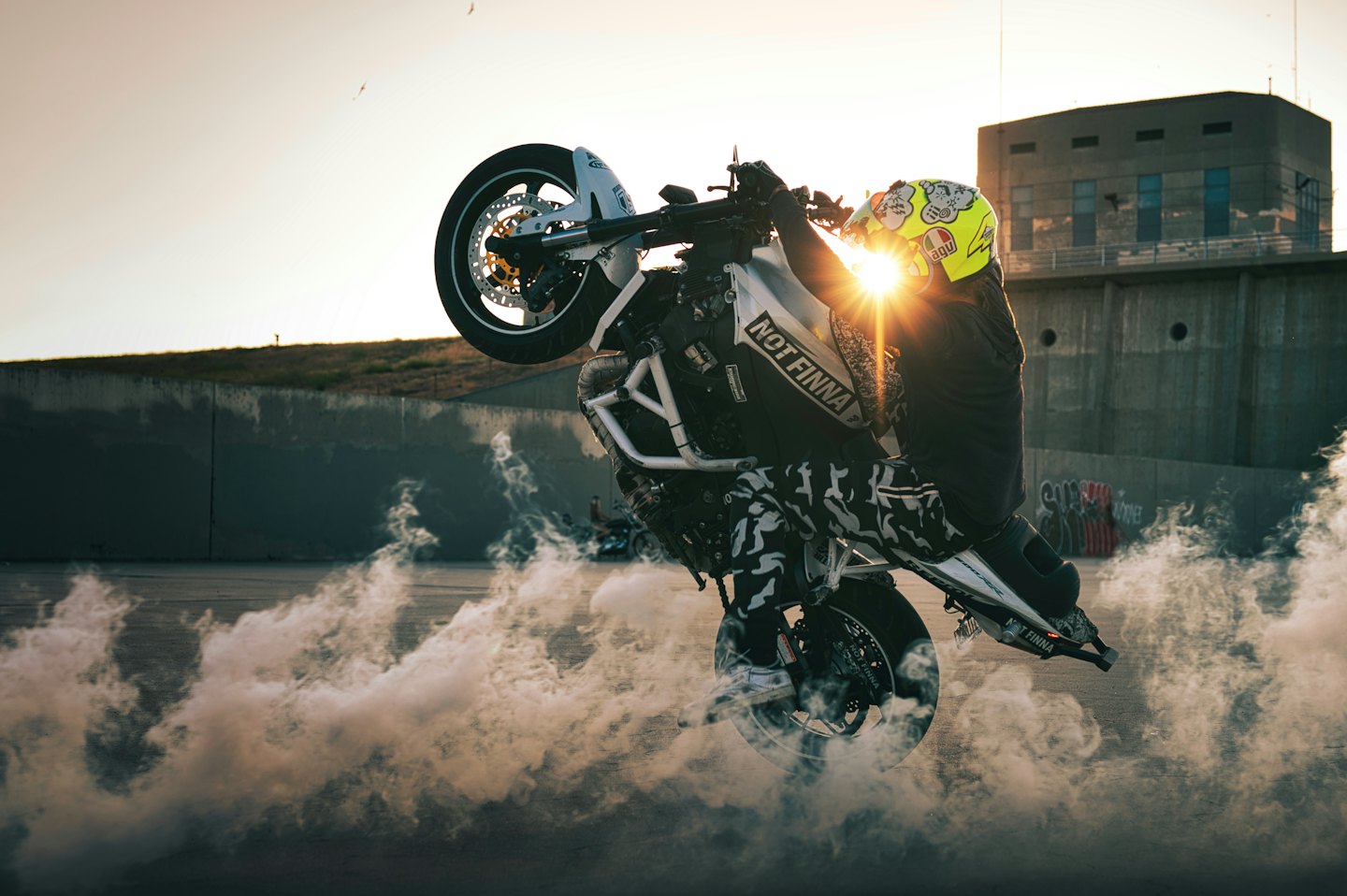 A stunt rider performs a wheelie on a smoking motorcycle.